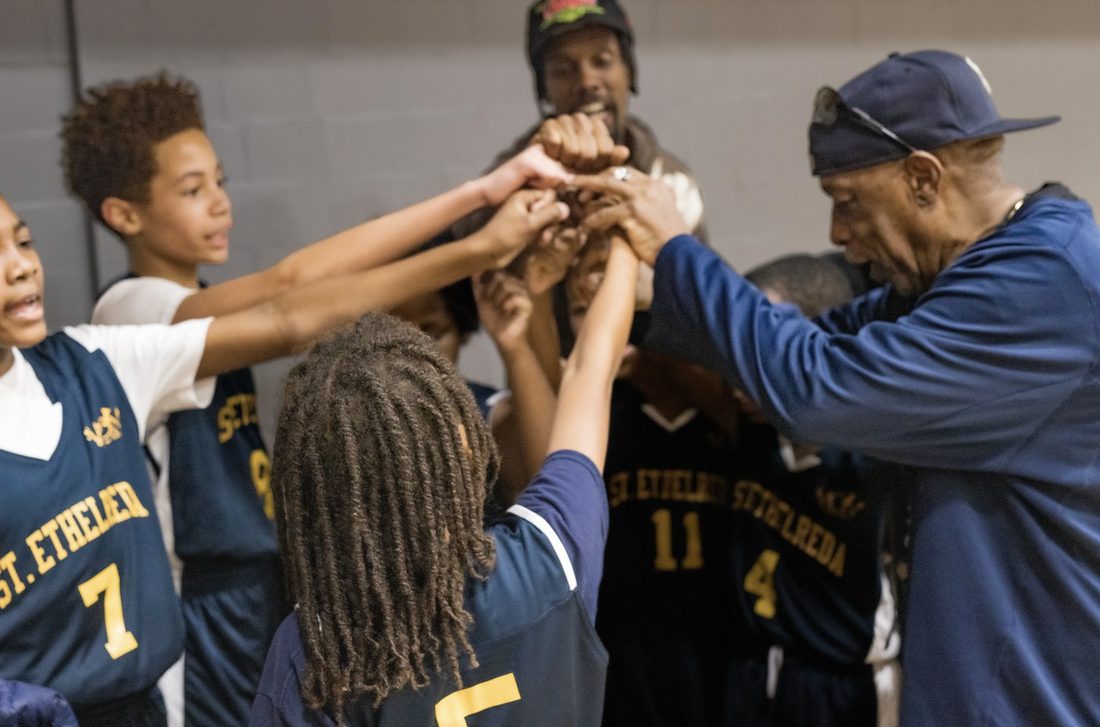 V.O.V basketball team putting their hands in during a huddle with their coach