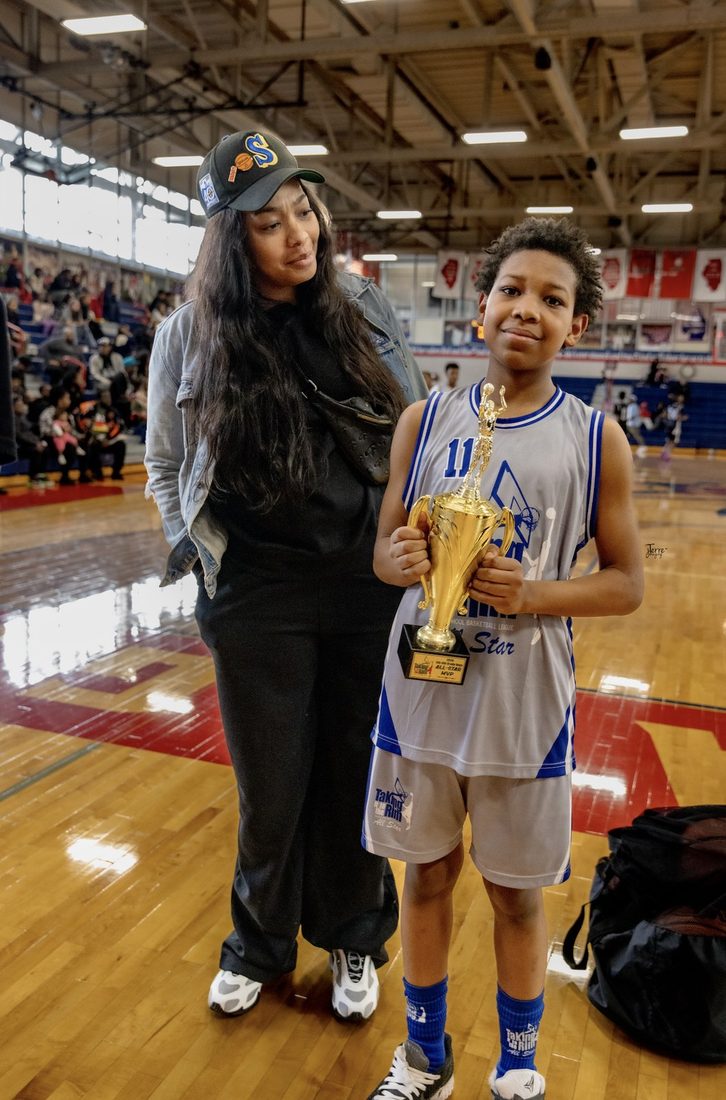 A young V.O.V All-Star holding his MVP trophy beside his mother