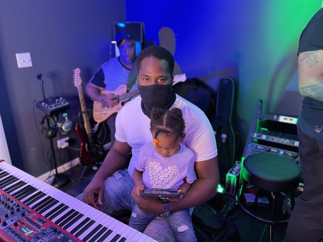 A V.O.V musician at the keys with his daughter on his lap in the studio